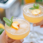 Two glasses of Peach Blossom Cosmo ready for a toast at a spring gathering.
