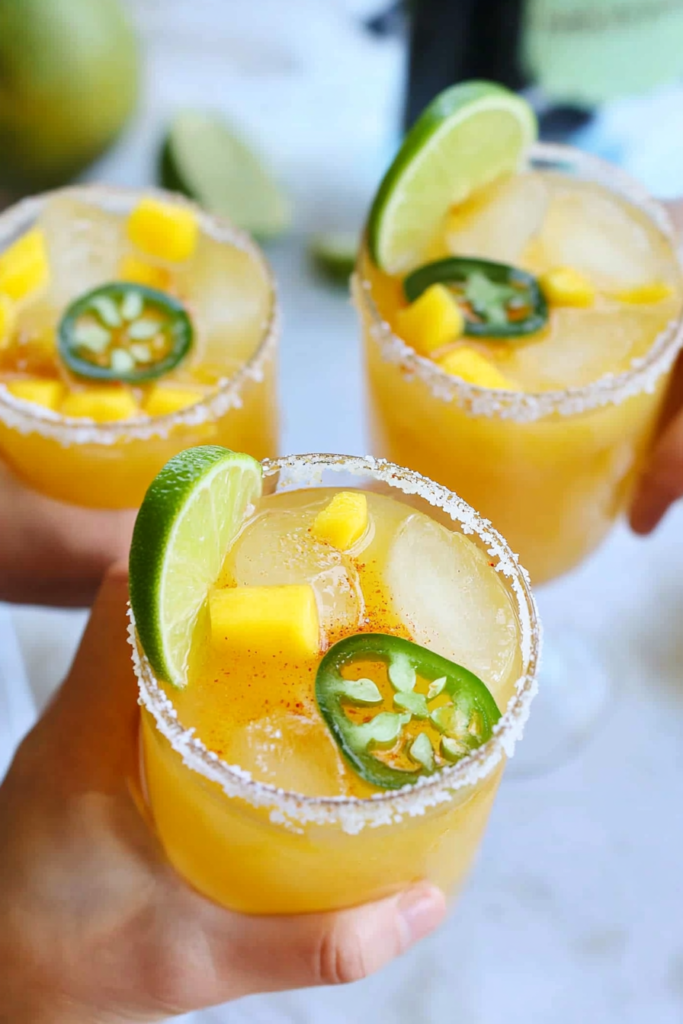 Pouring the strained Mango Jalapeño Margarita into a prepared rimmed glass filled with ice.