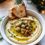 Lemon Artichoke Hummus served in a bowl with pita bread and vegetable sticks for dipping.