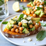 Assembling the Sweet Potato Toast by layering avocado and chickpea salad onto baked sweet potato slices.
