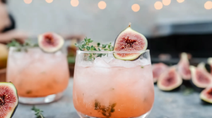 An elegant Fig Thyme Shrub Cocktail in a glass with ice, garnished with fresh figs and thyme.