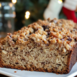 The whole Brown Butter Banana Bread loaf with coconut streusel topping, partially sliced on a cutting board.