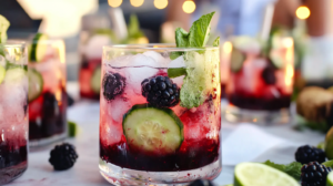 A tall, refreshing Blackberry Mint Gin Spritzer in a glass with ice, garnished with blackberries, mint, cucumber ribbons, and lime.