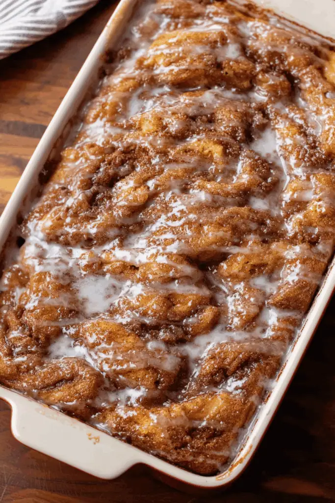 A 9x13 pan of golden-brown apple fritter cake, soaked in a white vanilla glaze and cut into squares.
