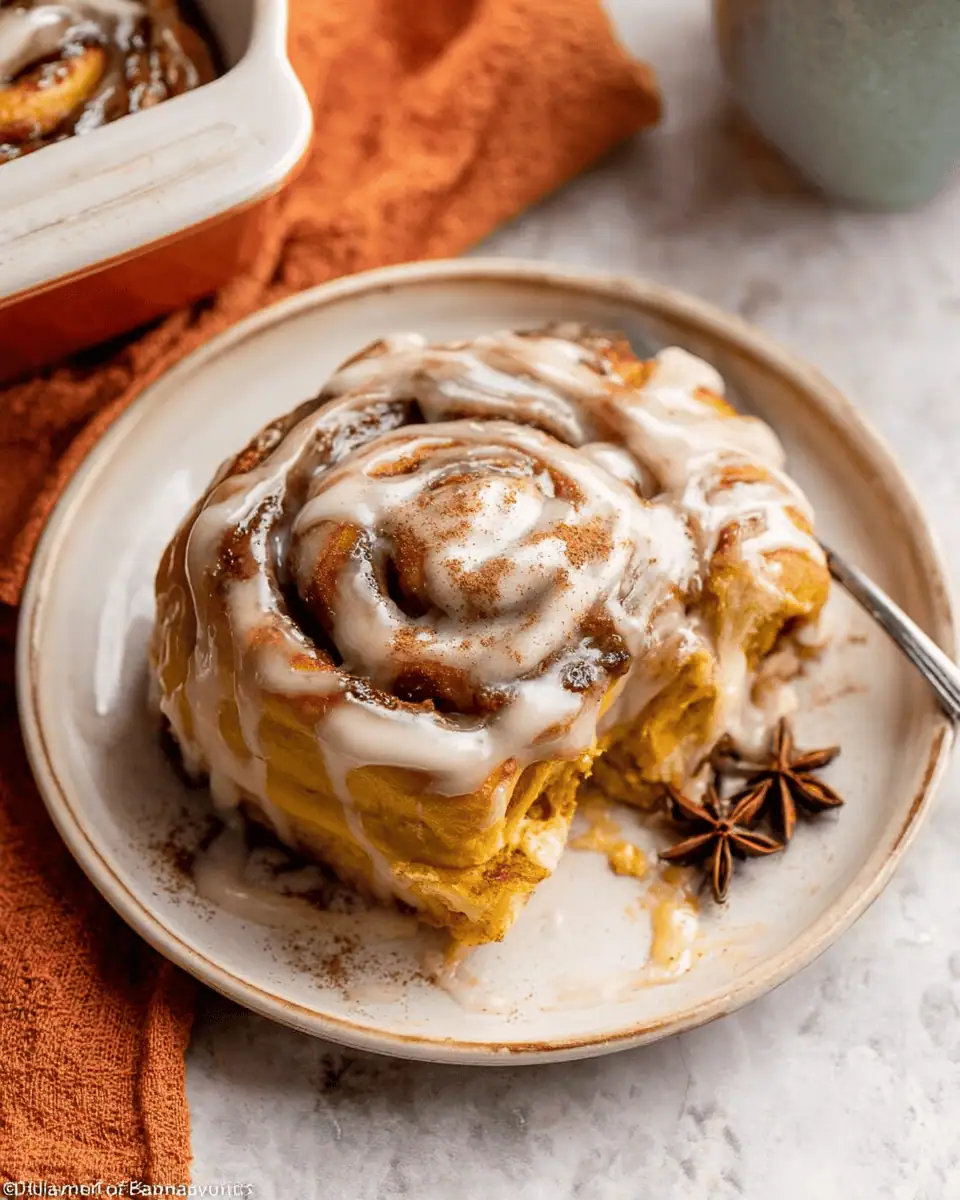 A close-up of a single, gooey pumpkin cinnamon roll on a plate, showing the frosting and soft spiral.