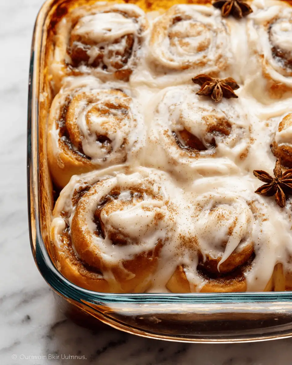 A hand pulling a single, gooey pumpkin cinnamon roll away from the others in the baking dish.