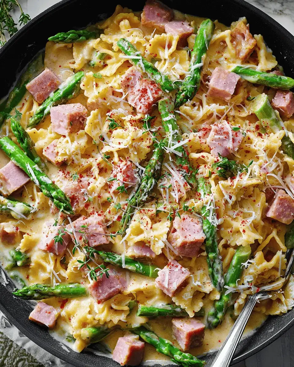 Creamy Ham Pasta with Asparagus: A 30-Minute Dinner 2 Shredded Parmesan being scattered over simmering heavy cream in a pan.